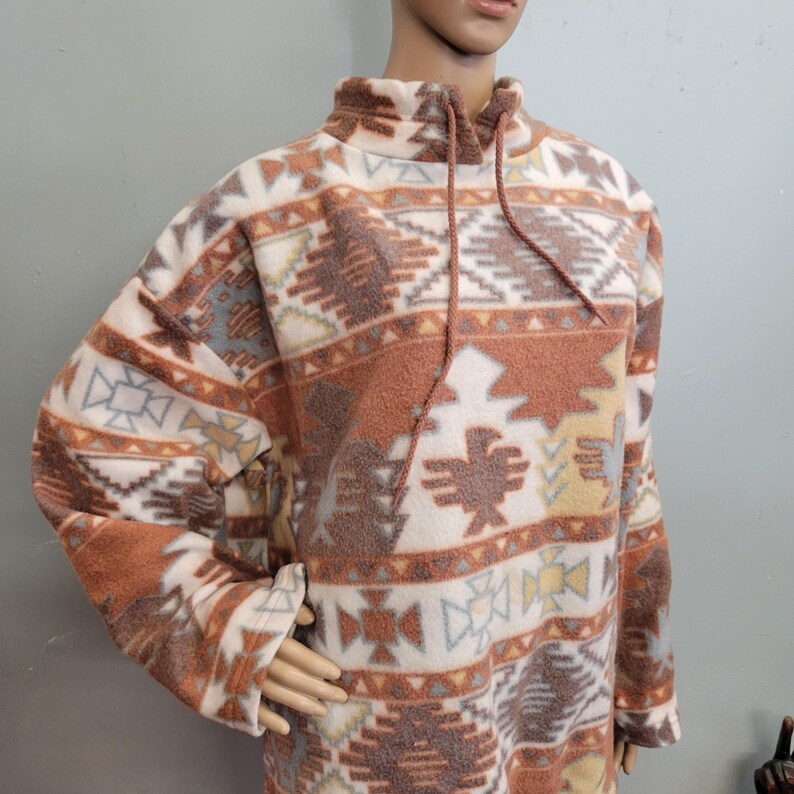 K&ouml;nnte beinhalten: Lang&auml;rmeliger Fleece-Pullover mit hohem Kragen und Kordelzug. Das Design zeigt ein Muster im S&uuml;dweststil mit geometrischen Formen und Vogelmotiven in Braun-, Creme-, Grau- und Gelbt&ouml;nen. Warmer und bequemer Pullover.