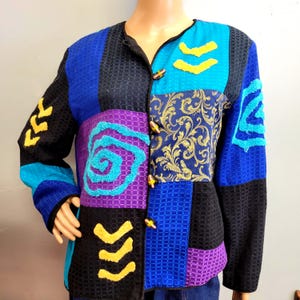 May include: A patchwork jacket with a variety of colors and textures. The jacket features a mix of blue, black, purple, and gold fabrics, with decorative yellow and turquoise accents. It has wooden button closures and a black trim.