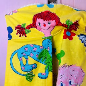 May include: A vintage yellow fabric featuring a cartoon doll and a blue lion. The doll has red pigtails and a pink face. The lion is blue with pink flower details. The fabric is decorated with floral patterns.
