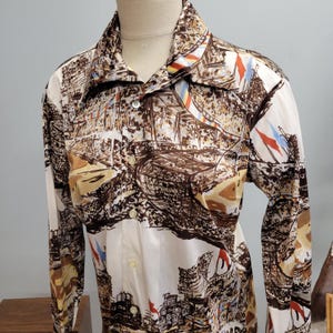 May include: A long-sleeved button-down shirt with a distinctive landscape print in shades of brown and beige, adorned with flags. The shirt, displayed on a mannequin, has a classic collar. The fabric appears to be lightweight.