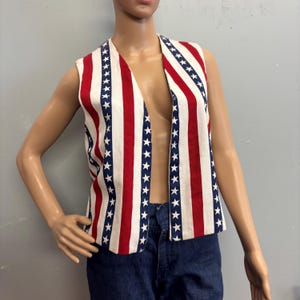 May include: A sleeveless vest with a patriotic design. The vest features alternating red and white stripes, with a row of blue stars along the edges. The vest is open in the front.