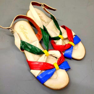May include: Pair of vintage cream-colored sandals with colorful accents. The sandals feature red, green, and blue straps, with yellow accents. The brand name "Softwear" is visible on the insole. The sandals have a small heel and ankle straps.