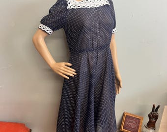 May include: A navy blue dress with white polka dots and white lace detailing. The dress features a square neckline and short sleeves. The dress is displayed on a mannequin.