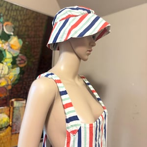 May include: A striped bucket hat and overalls set. The hat and overalls feature vertical stripes in red, white, blue, and green. The hat has a wide brim. The overalls have a bib and suspender straps.