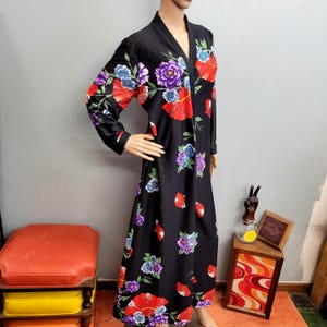 Puede incluir: Bata negra de manga larga con un estampado floral y de abanicos en rojo, morado y azul. La bata tiene cuello en V y un diseño largo hasta el suelo. El estampado floral se repite por toda la bata.