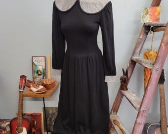 May include: A black vintage dress with a contrasting white and black checked collar and cuffs. The long-sleeved dress has a fitted bodice and a flowing skirt, displayed on a mannequin. A classic style.