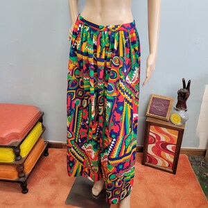 May include: A pair of wide-leg trousers featuring a vibrant, multi-colored geometric and paisley-inspired pattern in shades of red, yellow, green, blue, and white. The garment has a high-waisted fit with a gathered, pleated waistband design.