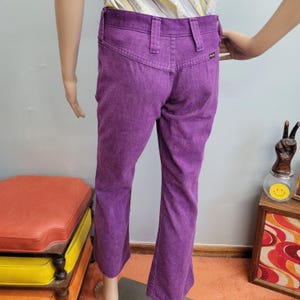 May include: A pair of vintage purple corduroy pants. The pants have a high waist, belt loops, and a flared leg. The back pockets are visible. The pants are displayed on a mannequin.