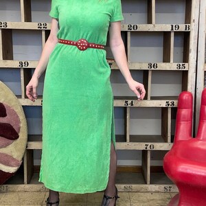 Puede incluir: Un vestido maxi verde con capucha, una abertura lateral y un cintur&oacute;n rojo con tachuelas. El vestido est&aacute; hecho de un tejido suave de toalla.