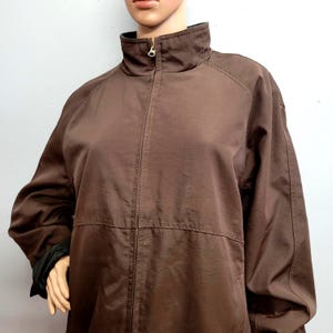 May include: A brown zip-up jacket with a high collar. The jacket has a full-length zipper and long sleeves. The cuffs are black. The jacket is made of a smooth, lightweight material.