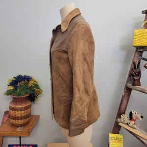 May include: A brown suede jacket with a brown leather collar and trim. The jacket has a button closure and two pockets.