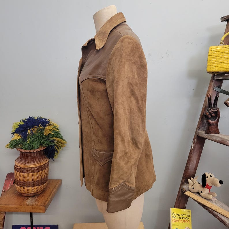 May include: A brown suede jacket with a brown leather collar and trim. The jacket has a button closure and two pockets.