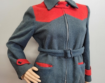 May include: A vintage wool jacket in a dark teal color with red accents. The jacket features a red yoke, pocket trim, and cuff details. It has a zip-up front, a belt with a buckle, and a classic collar. The jacket is displayed on a mannequin.
