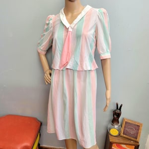 May include: A vintage two-piece dress with vertical stripes in pastel pink, mint green, and white. The top has a white collar and short, puffed sleeves. A matching pink scarf is tied at the neckline. The skirt is knee-length.