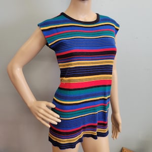 Puede incluir: Una camiseta sin mangas a rayas en una variedad de colores, incluyendo azul, rojo, amarillo, verde y negro. La camiseta se muestra en un maniquí. La camiseta tiene un cuello redondo y rayas horizontales. La camiseta está hecha de punto.