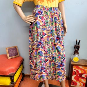 May include: A midi-length skirt featuring a vibrant, multi-coloured comic book print with various rectangular panels. The skirt has a high waist with an elastic band and a vertical row of five round, light-coloured buttons running down the front centre.