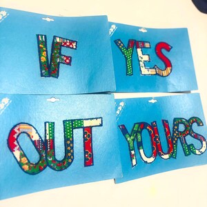 May include: Four rectangular light blue display cards featuring fabric-covered letters. The letters spell out IF, YES, OUT, and YOURS. Each letter is crafted from various colorful patterned fabrics, including floral, plaid, and striped designs.