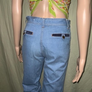 May include: Light blue denim pants with dark blue pocket accents and a button closure. The pants have a classic, straight-leg fit and a high waist. The back pockets are rectangular with a dark blue trim.