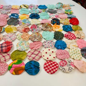 May include: A collection of colorful, fabric yo-yos in various patterns and colors, including floral, polka dot, and plaid. The yo-yos are arranged closely together, creating a patchwork effect. The colors include red, blue, green, pink, and yellow.