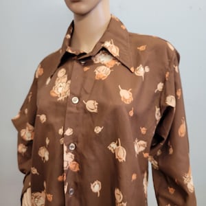 May include: Brown button-up shirt featuring a floral design in peach and cream hues. The shirt has a wide collar and long sleeves. The fabric appears to be smooth, possibly synthetic.