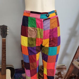 May include: High-waisted pants featuring a multi-colored patchwork design with square fabric panels in shades of red, yellow, green, blue, purple, orange, and pink. The pants include a single dark button closure at the center front waistband.