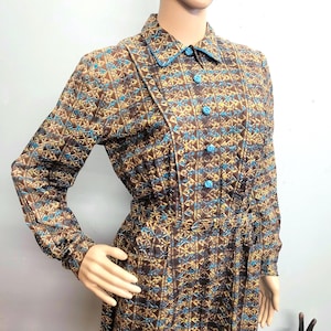 May include: A vintage dress featuring a geometric pattern in brown, gold, and teal. The long-sleeved dress has a collared neckline, teal buttons, and a fitted waist. The dress is displayed on a mannequin.