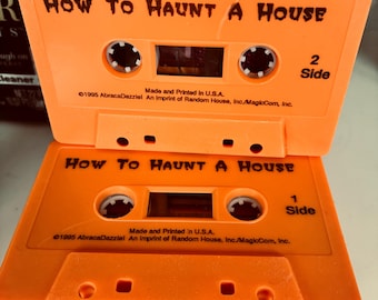 May include: Two bright orange cassette tapes labeled How To Haunt A House. Each tape features black text, white spools, and the printed details: Made and Printed in U.S.A., 1995 AbracaDazzle! An imprint of Random House, Inc./MagicCom, Inc. Side 1 and 2.