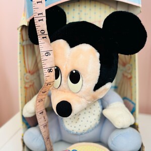 May include: A vintage Mickey Mouse plush toy, primarily light blue and cream-colored, with black ears and a black nose. The toy is approximately 8 inches tall, and is in its original box. The plush has a bib with blue polka dots.