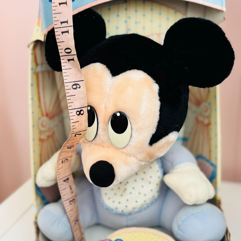 May include: A vintage Mickey Mouse plush toy, primarily light blue and cream-colored, with black ears and a black nose. The toy is approximately 8 inches tall, and is in its original box. The plush has a bib with blue polka dots.