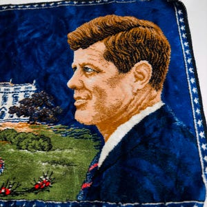May include: A vintage tapestry depicting a man in a blue suit, white shirt and red tie. The background is a deep blue with a depiction of the White House and a green lawn. The tapestry has a decorative border. The portrait is in profile.