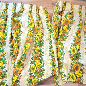 May include: Two floral print curtain panels. The curtains feature a cream background with a repeating pattern of yellow and orange sunflowers, green leaves, and small red berries. The curtains are made of a lightweight fabric.