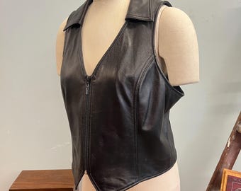 May include: A black leather vest with a V-neck collar and a full-length zipper. The vest is sleeveless and has a tailored fit. The garment is displayed on a mannequin.