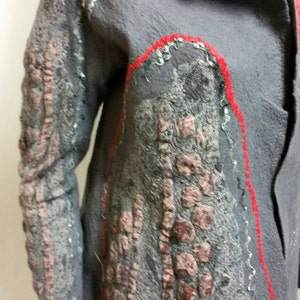 May include: A gray felted jacket with red and silver embroidery. The jacket has a collar and a button closure. The embroidery is in the shape of a flower.