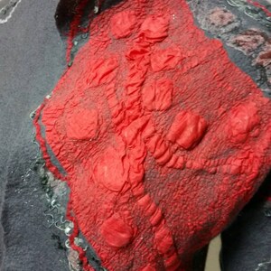 May include: A gray wool jacket with a red felt applique. The applique has a textured, bumpy surface and is shaped like a heart.
