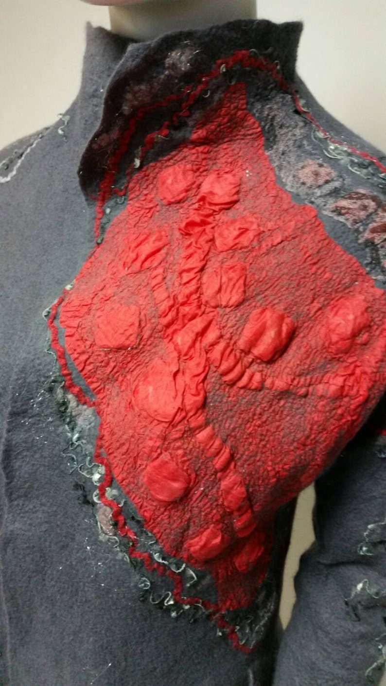 May include: A gray wool jacket with a red felt applique. The applique has a textured, bumpy surface and is shaped like a heart.