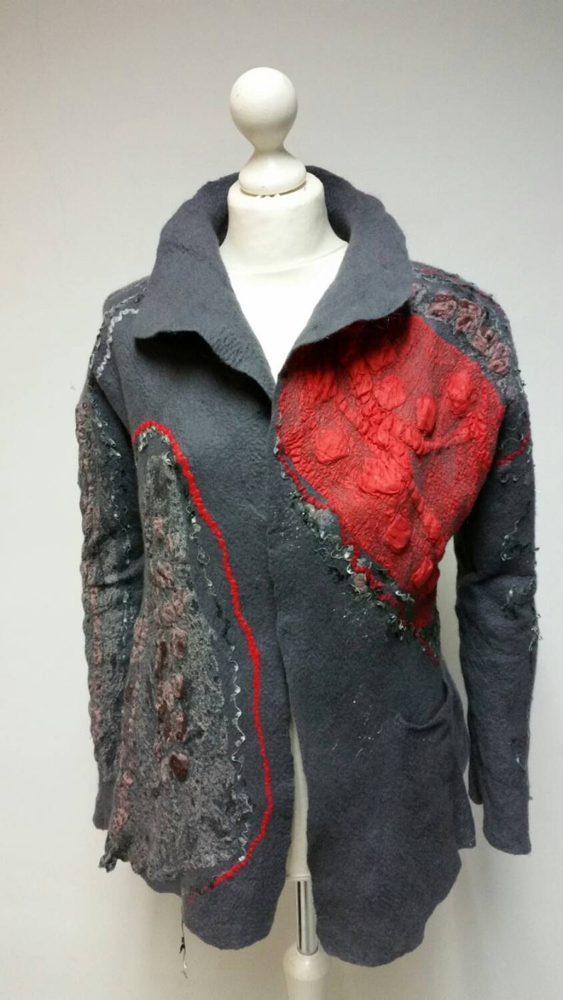 May include: A gray wool jacket with red and gray felt applique details. The jacket has a collar and long sleeves.