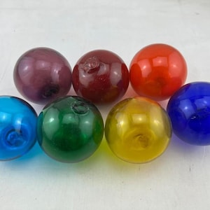May include: Six glass balls in various colors, including blue, green, yellow, red, purple, and dark blue. The balls are round and smooth, and they are all about the same size.