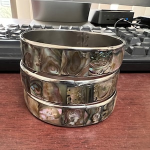 May include: Three silver bangles with a mother-of-pearl inlay. The bangles are stacked on top of each other.
