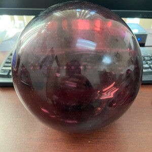 May include: A large, round, purple glass ball. The ball is smooth and shiny, and it reflects the light.