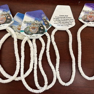 May include: Four white shell necklaces with a tag that reads "Genuine Shell Jewelry" and the text "Genuine Shell is a precious gift of nature. Its unique, rare and glossy luster is reflecting constituent colors of the sunlight and making your ordinary and extraordinary, today and everyday."