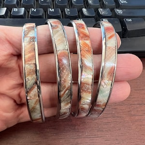 May include: Four silver bangles with a mother-of-pearl inlay. The inlay is a mix of white, brown, and orange.