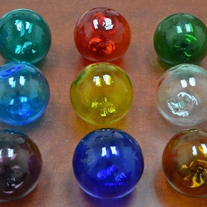 May include: Nine glass floats in various colors, including green, red, blue, yellow, clear, brown, and purple. The floats are round and have a smooth, shiny surface.