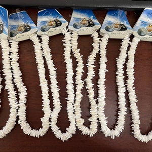 May include: Six white shell necklaces with a blue and white tag that says "Genuine Shell Jewelry".