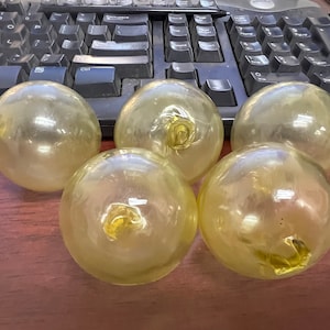 May include: Five translucent yellow glass spheres, each with a slightly different shape and texture, are arranged on a wooden surface.