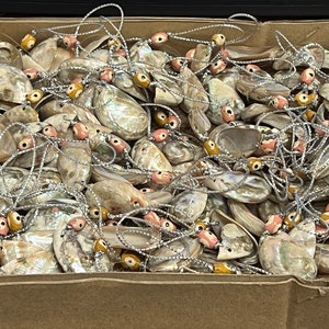 May include: A box filled with a large quantity of iridescent seashell ornaments. Each ornament is strung with a silver cord and features a variety of colorful beads.