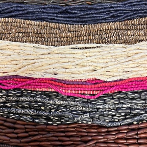 May include: Multiple strands of beads arranged in horizontal rows. The collection includes dark brown cylindrical beads, navy blue discs, tan patterned discs, cream-colored carved tubes, pink and purple discs, black patterned tubes, and brown oval beads.