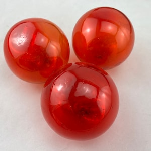 May include: Three red glass balls with a shiny, reflective surface. The balls are arranged in a triangular shape.