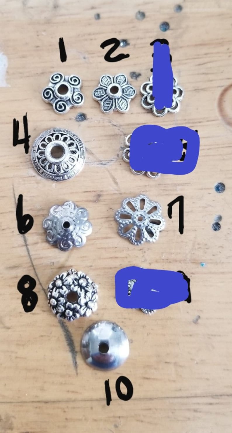 May include: Ten silver metal beads with different designs, numbered 1 through 10. The beads are arranged in a row on a wooden surface.