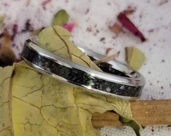 May include: A silver ring with a black and white inlay. The ring is on a yellow leaf.