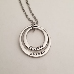May include: A silver necklace with two interlocking circles. The circles are engraved with the names "ELLISYN" and "GRAHAM".